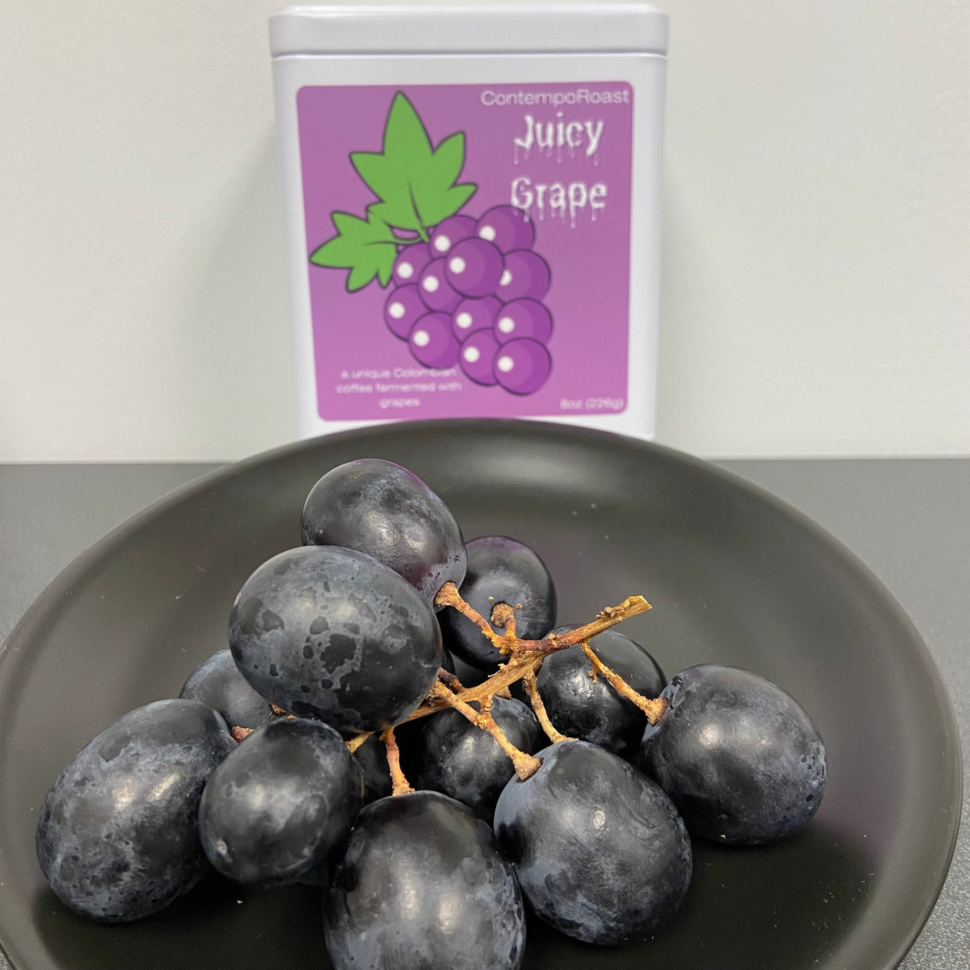 Bunch of dark purple grapes in front of a keepsake tin of Juicy Grape coffee in the background