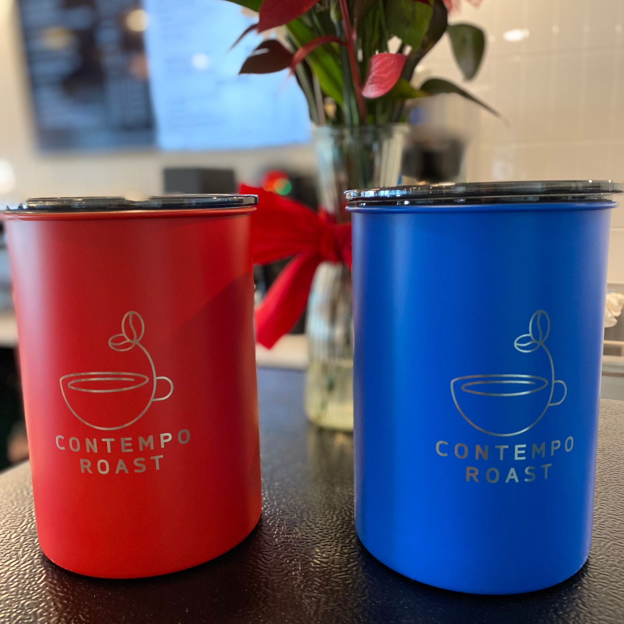 matte red and matte blue canisters with ContempoRoast etched on fronts sitting in a coffee shop