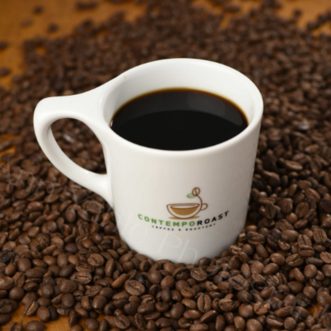 white porcelain mug with ContempoRoast Coffee & Roastery logo on a background of roasted coffee beans